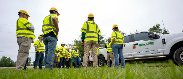 Several members of the Row-Care team wear their neon yellow safety vests and hard hats and stand in a circle, speaking with each other.