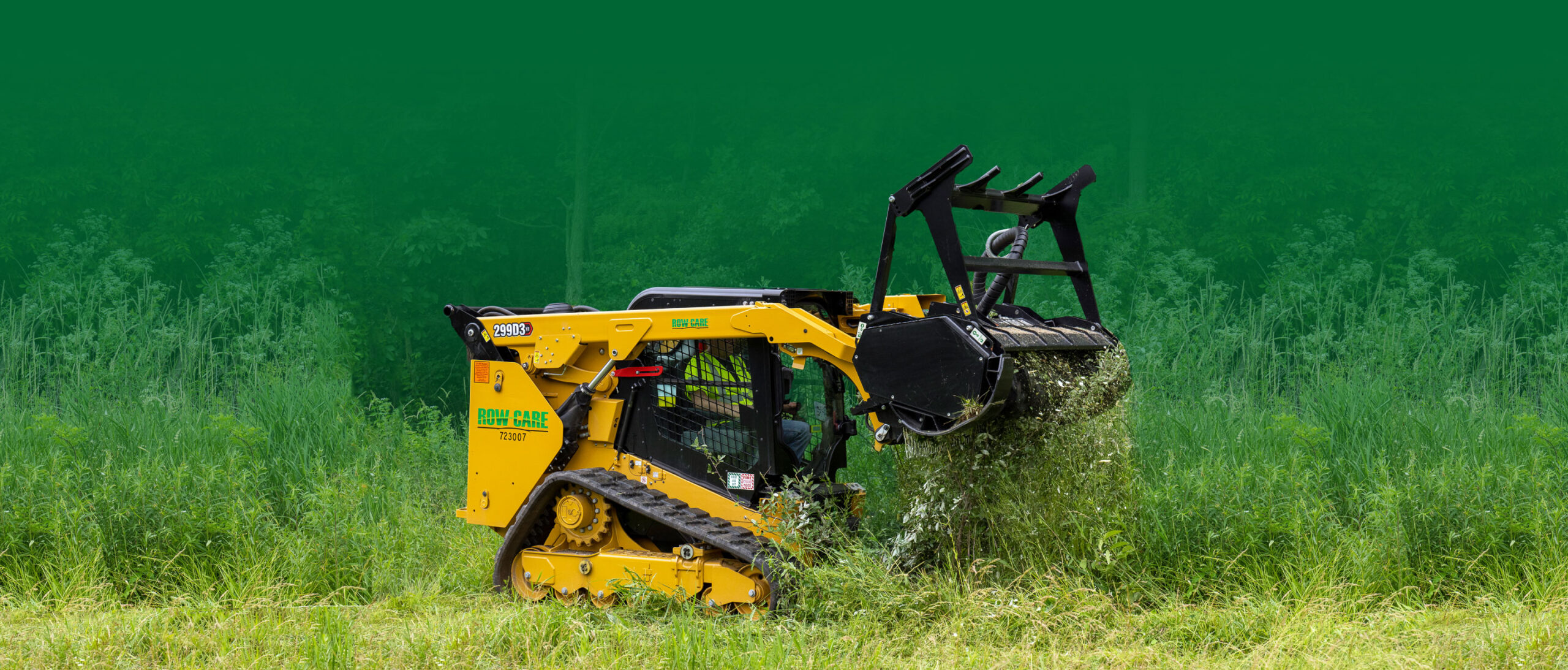 A branded yellow commercial skid steer with mulcher clears a path in a field with brush.