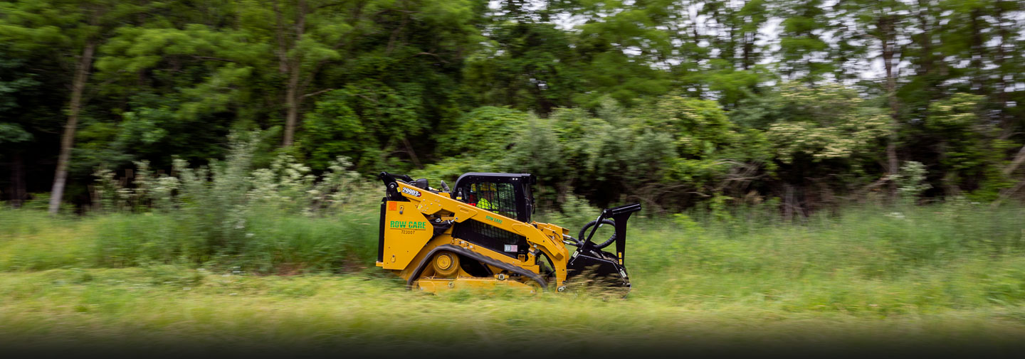 A commercial skid steer drives through a field of grass.